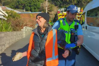 Rosemary Penwarden is led away by police after gluing her hand to a road in New Zealand to stop traffic as part of a protest by Restore Passenger Rail in August 2023. Credit: Photo Courtesy Restore Passenger Rail