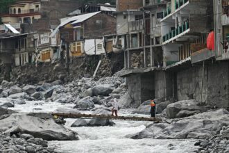 In a photo taken on May 4, 2023, residents cross a temporary bridge near hotels and houses that were damaged by flash floods on the banks of the Swat River in 2022 in Bahrain, a town in the Swat valley in Khyber Pakhtunkhwa province of Pakistan, which was lashed by unprecedented monsoon rains over the summer of 2022. The ensuing floods that put a third of the country underwater, damaged two million homes and killed more than 1,700 people. Credit: Aamir Qureshi / AFP via Getty Images