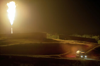 A truck filled with gas departs a newly completed gas well. The flare is burning because the infrastructure to transport the gas via pipelines was not yet complete. Credit: Scott Goldsmith