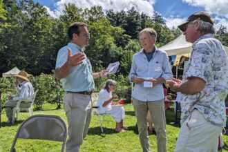 Seth Berry, left, an author of the Pine Tree Power proposal and a former Democratic state representative, answers questions from potential voters at a gathering of climate activists at a home in Winslow, Maine, in August. Credit: Annie Ropeik
