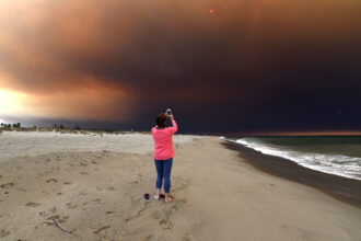 Smoke from Southern California wildfires moves towards the Pacific Ocean, creating spectacular dark skies as a local on Oxnard Shores Beach California captures the moment on Nov. 9, 2018. Credit: Paul Harris/Getty Images