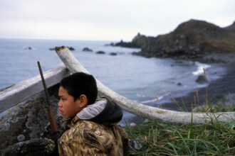 Steven James, 12, waits to hunt geese on St. Lawrence Island, in Alaska, sitting hidden behind a wood bar and a whale bone. Credit: Ann Johansson/Corbis via Getty Images.