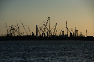 Construction cranes stand silhouetted by the sunset at the Golden Pass LNG Terminal in Sabine Pass, Texas, in April 2022. Golden Pass LNG, a joint venture between ExxonMobil and Qatar Petroleum, began as an import terminal and construction seen today will create export capability. Credit: The Washington Post via Getty Images