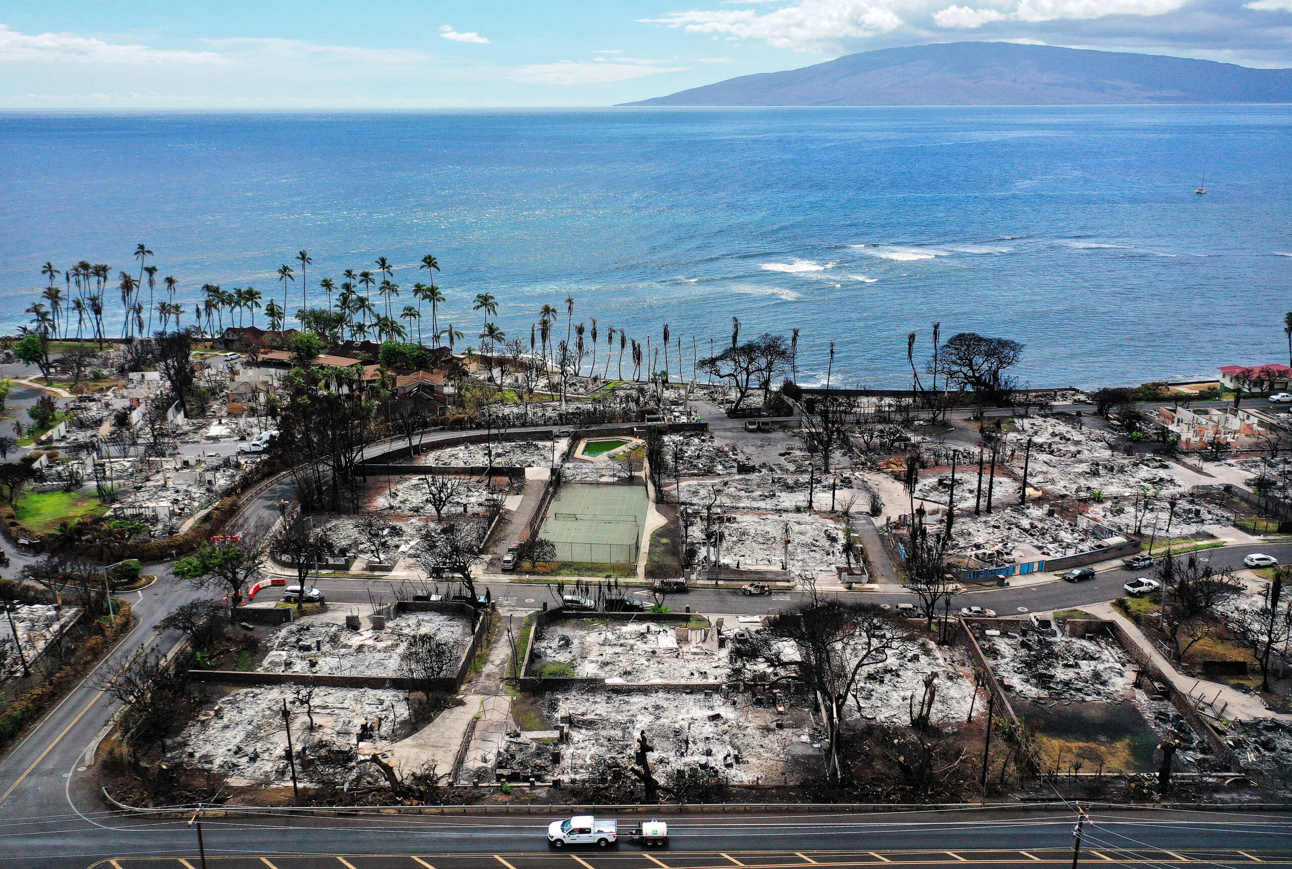 In an aerial view, a recovery vehicle drives past burned structures and cars two months after a devastating wildfire on October 9, 2023 in Lahaina, Hawaii. Credit: Mario Tama/Getty Images