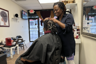 Yakini Horn, owner of Yaya’s Natural Hair Boutique in Atlanta, rolled sections of Akeyla Peele-Tembong’s hair in her hands during a styling visit on Feb. 20, 2023. Horn was creating “starter locs,” the early stage of a natural hairstyle that will take months to root. Credit: Victoria St. Martin